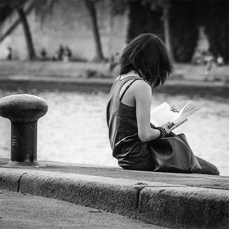 Photo d'une femme en noir et blanc lisant sur un quai parisien